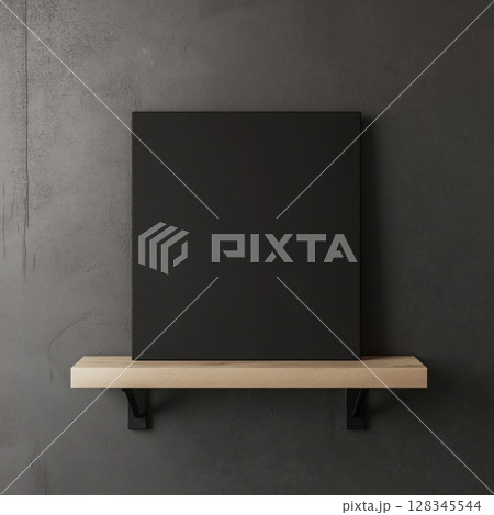 blank black canvas hanging on a wooden shelf against a gray concrete wall. The canvas is rectangular in shape and appears to be made of a light-colored wood	 128345544