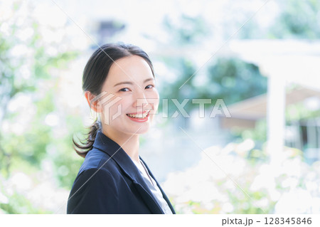 綺麗な逆光の新緑の中でパソコンを持つスーツの女性のカメラ目線ビジネスシーン 128345846