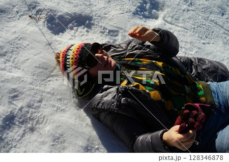 Woman Relaxing on Snow in Colorful Winter Outfit Woman Relaxing on Snow in Colorful Winter Outfit 128346878