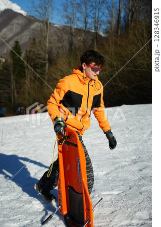 Teen Carrying Sledge in Snowy Mountain Setting Teen Carrying Sledge in Snowy Mountain Setting 128346915