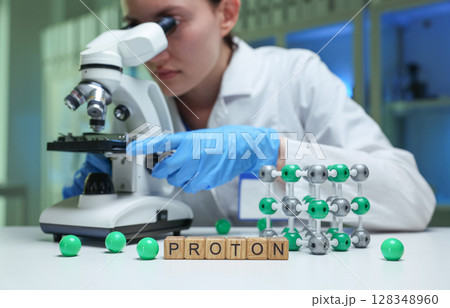 A scientist observing protons through a microscope in a lab for research and discovery A scientist observing protons through a microscope in a lab for research and discovery 128348960