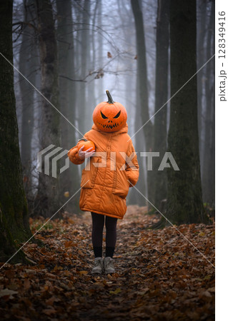 Girl in orange coat poses with scary jack-o'-lantern head Girl in orange coat poses with scary jack-o'-lantern head 128349416
