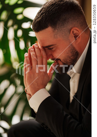 A serious, thoughtful man with hands to the face in a business suit is sitting 128350659