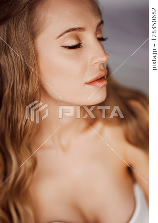 Sensual portrait of a sexy blonde young woman in a white off-the-shoulder dress. Sensual portrait of a sexy blonde young woman in a white off-the-shoulder dress. 128350682