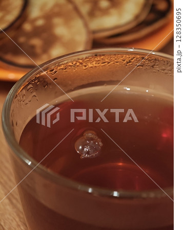 Warm tea with bubbles beside delicious pancakes on a rustic wooden table in a cozy kitchen setting 128350695