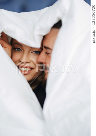 A man and a woman under the blanket on a bed. 128350720