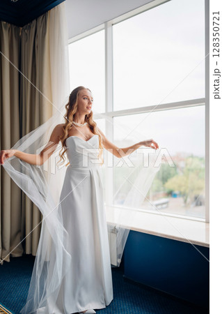 The bride standing by the window. simple beautiful elegant wedding dress The bride standing by the window. simple beautiful elegant wedding dress 128350721