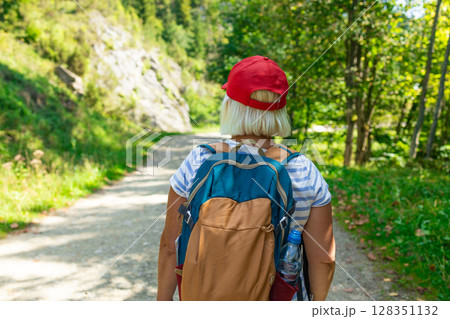 Senior Woman Walking on Forest Trail with Backpack Senior Woman Walking on Forest Trail with Backpack 128351132