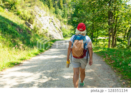 Senior Woman Walking on Forest Trail with Backpack 128351134