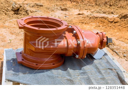 Large, orange pipe fire fitting rests waiting to be installed on wooden platform at construction site under works day 128351448