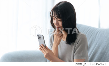 ソファに座ってスマートフォンを使う笑顔の女性 ソファに座ってスマートフォンを使う笑顔の女性 128352677