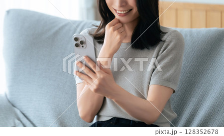 ソファに座ってスマートフォンを使う笑顔の女性 ソファに座ってスマートフォンを使う笑顔の女性 128352678