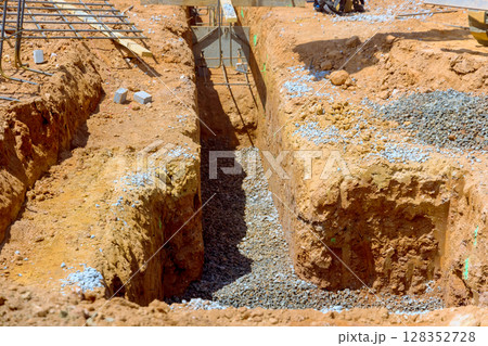 Construction workers prepare trenches filled with gravel for building foundations in rural area under works day Construction workers prepare trenches filled with gravel for building foundations in rural area under works day 128352728
