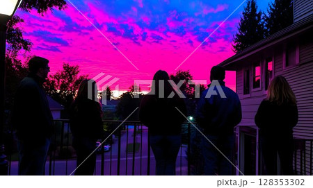 Silhouetted figures watching vibrant sunset sky over houses 128353302