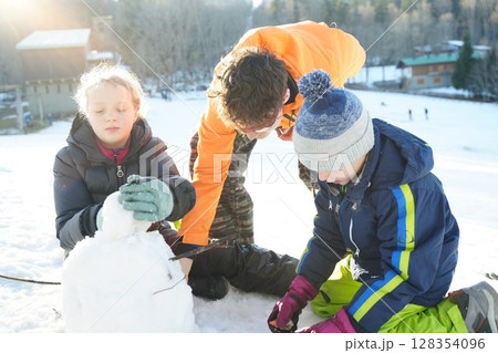 Children Building a Snowman on a Sunny Winter Day Children Building a Snowman on a Sunny Winter Day 128354096