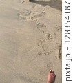 Textured sandy beach ground with many footprints and a single foot. 128354187