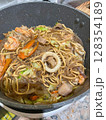 A savory, stir-fried noodle dish with shrimp, squid, meat, and fresh vegetables cooked in a pan. 128354189