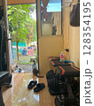 Adorable cat patiently sits in an open doorway, gazing at the lush green backyard. 128354195