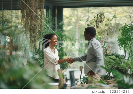 Handshake between professionals in a lush, plant-filled eco-office with natural daylight. Perfect 128354252