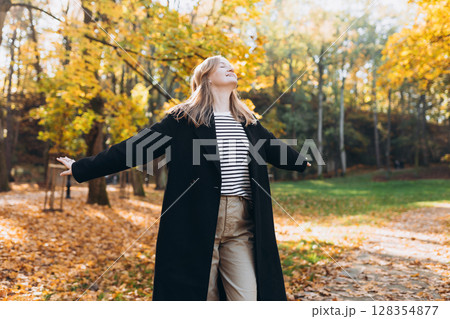 30s blonde Girl in motion expressing happiness at city park. Attractive, cheerful happy woman raising hands up, feeling free and joyful during the nice autumn day. 128354877