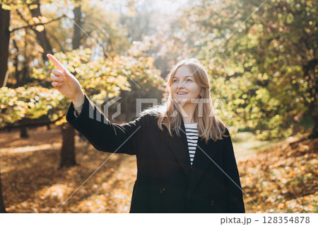 Woman pointing finger something in park during autumn. . Autumn landscape, calmness, tranquility concept. Pretty female standing on nature background. High quality photo. 128354878