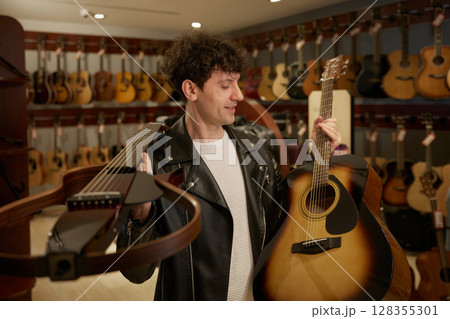 A man in a stylish leather jacket holds guitars A man in a stylish leather jacket holds guitars 128355301
