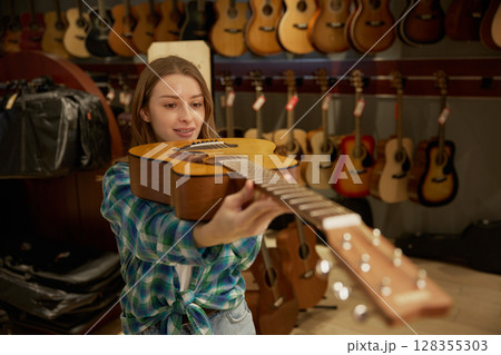 A woman is holding a guitar in front of a wall of guitars A woman is holding a guitar in front of a wall of guitars 128355303
