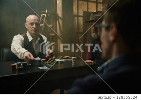 Intense poker and card game in a smoky room between male company Intense poker and card game in a smoky room between male company 128355324