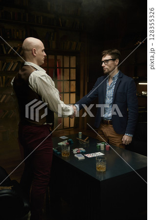 Two skilled players finalize an deal at poker table surrounded by colorful chips and cards 128355326