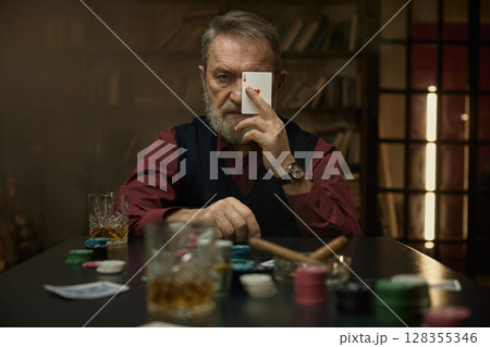 A focused gentleman with a groomed beard holds a playing card A focused gentleman with a groomed beard holds a playing card 128355346