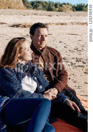 Loving couple walks on beach along sea on sunny autumn day. Weekend and lifestyle concept. Vertical photo. High quality photo Loving couple walks on beach along sea on sunny autumn day. Weekend and lifestyle concept. Vertical photo. High quality photo 128356416