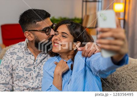 Indian family couple man woman taking selfie on smartphone with kiss on cheek, romantic fun moment Indian family couple man woman taking selfie on smartphone with kiss on cheek, romantic fun moment 128356495