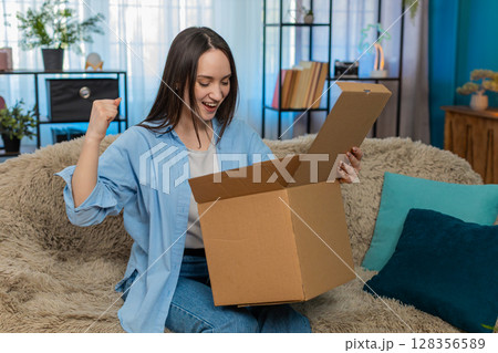Woman happily unpacking delivered box pleasantly surprised excitedly holding desired new purchase Woman happily unpacking delivered box pleasantly surprised excitedly holding desired new purchase 128356589