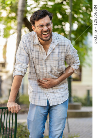 Indian young man traveler feeling sudden strong abdominal stomach ache, gastritis problem on street 128356684