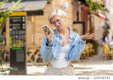 Upset young woman using cellphone typing browsing, loses becoming shocked bad news on city street 128356741
