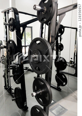 Weightlifting equipment with black plates arranged on a rack in a modern gym environment Weightlifting equipment with black plates arranged on a rack in a modern gym environment 128356957
