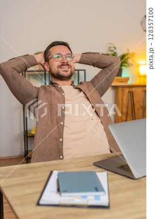 Happy Caucasian young businessman closing laptop after finishing work relaxing at home office desk 128357100