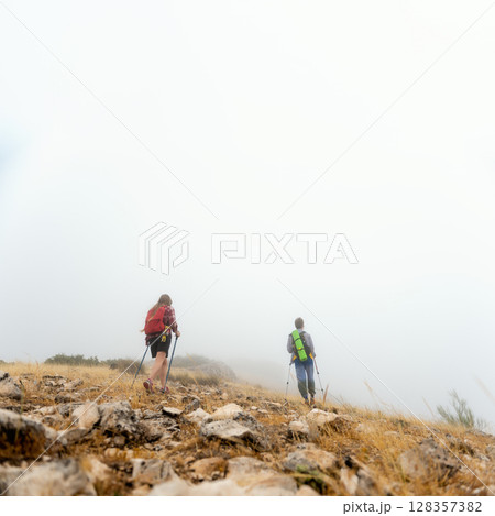 Foggy Morning Hike in the Mountains Featuring Two Travelers Trekking Uphill in a Serene Natural Landscape 128357382