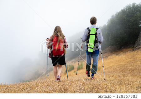 Two Hikers Navigating Through a Foggy Landscape in the Early Morning 128357383