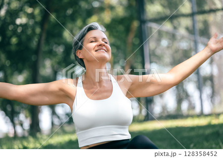 Happy Mature Woman Embracing Nature with Open Arms in a Peaceful Outdoor Forest Setting Happy Mature Woman Embracing Nature with Open Arms in a Peaceful Outdoor Forest Setting 128358452