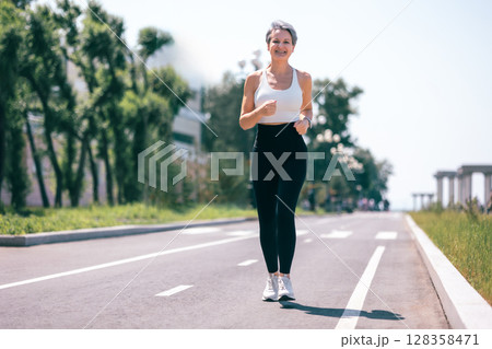 Happy Mature Woman Jogging Outdoors in Activewear on Sunny Day in Urban Park Environment 128358471