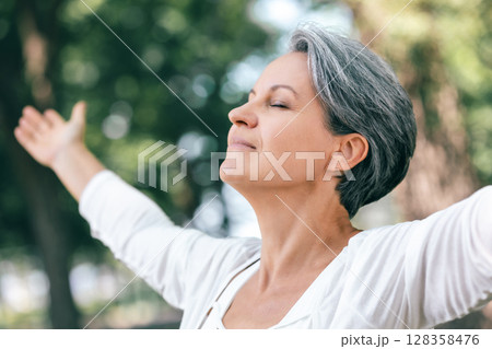 Peaceful Mature Woman with Closed Eyes Embracing Nature and Mindfulness in the Forest Peaceful Mature Woman with Closed Eyes Embracing Nature and Mindfulness in the Forest 128358476