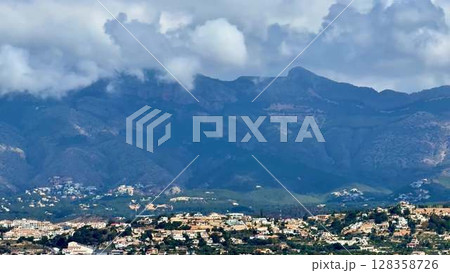 A stunning view of majestic mountains with dramatic clouds over charming houses in a serene setting A stunning view of majestic mountains with dramatic clouds over charming houses in a serene setting 128358726