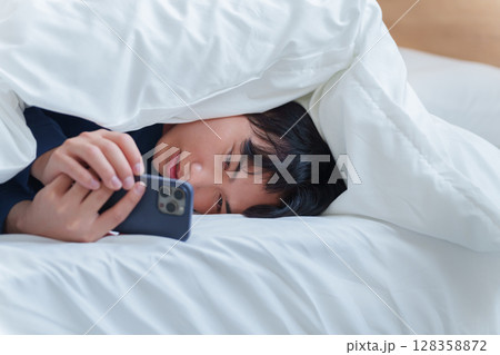 ベッドでスマホを使う男性 128358872