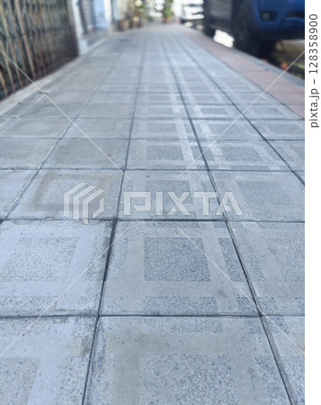 Grey concrete tiled sidewalk with square pattern stretches down an empty urban street into distance, creating powerful perspective of depth and conveying feeling of solitude Grey concrete tiled sidewalk with square pattern stretches down an empty urban street into distance, creating powerful perspective of depth and conveying feeling of solitude 128358900