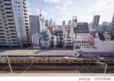 【日本】ビルの高層階から望む東京23区の街並みと黄色いラインの入ったJR総武線の電車 128358960