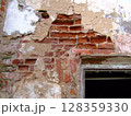 The textured surface reveals peeling plaster and exposed bricks, highlighting the decay in an old, abandoned structure. Sunlight subtly filters in through an opening, enhancing the scene's atmosphere. 128359330