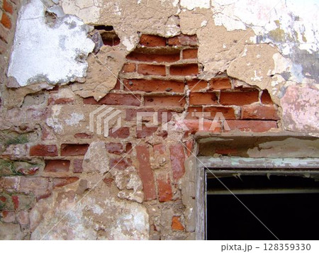 The textured surface reveals peeling plaster and exposed bricks, highlighting the decay in an old, abandoned structure. Sunlight subtly filters in through an opening, enhancing the scene's atmosphere. The textured surface reveals peeling plaster and exposed bricks, highlighting the decay in an old, abandoned structure. Sunlight subtly filters in through an opening, enhancing the scene's atmosphere. 128359330