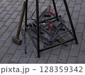 A collection of metal tools and hardware is displayed on a black iron stand in a workshop space. The tools show signs of use, reflecting a working environment. 128359342