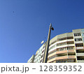 A residential building stands under a bright blue sky, with a streetlight and satellite dish visible. This captures vibrant urban life in a daylight setting, highlighting city design. 128359352